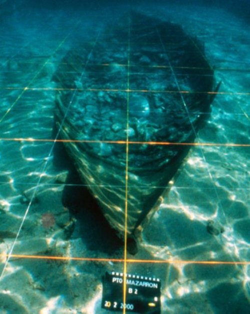 An underwater photo of a shipwreck of a small boat, covered by gridlines