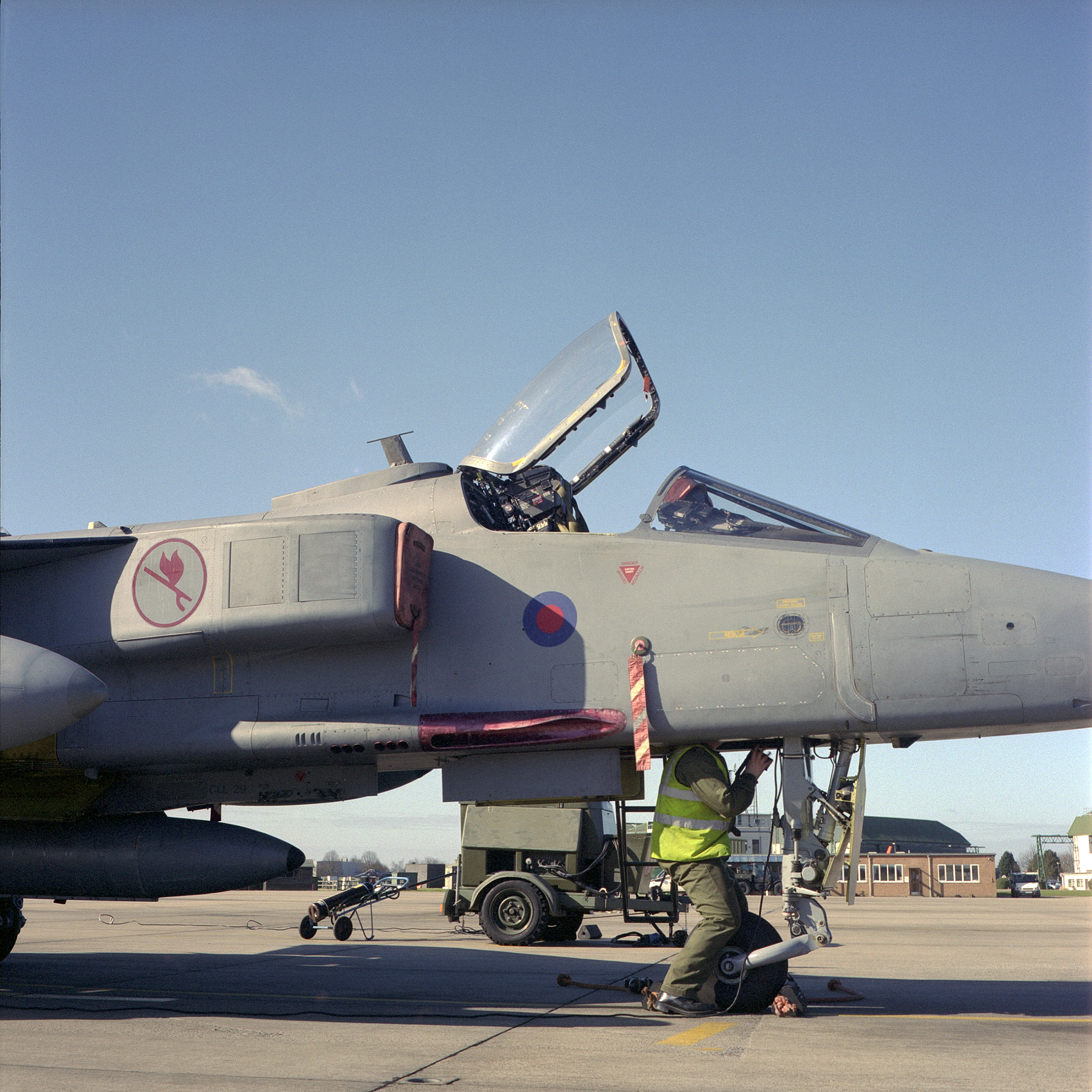 Man in hi-vis jacket with head disappearing up into fighter place cockpit
