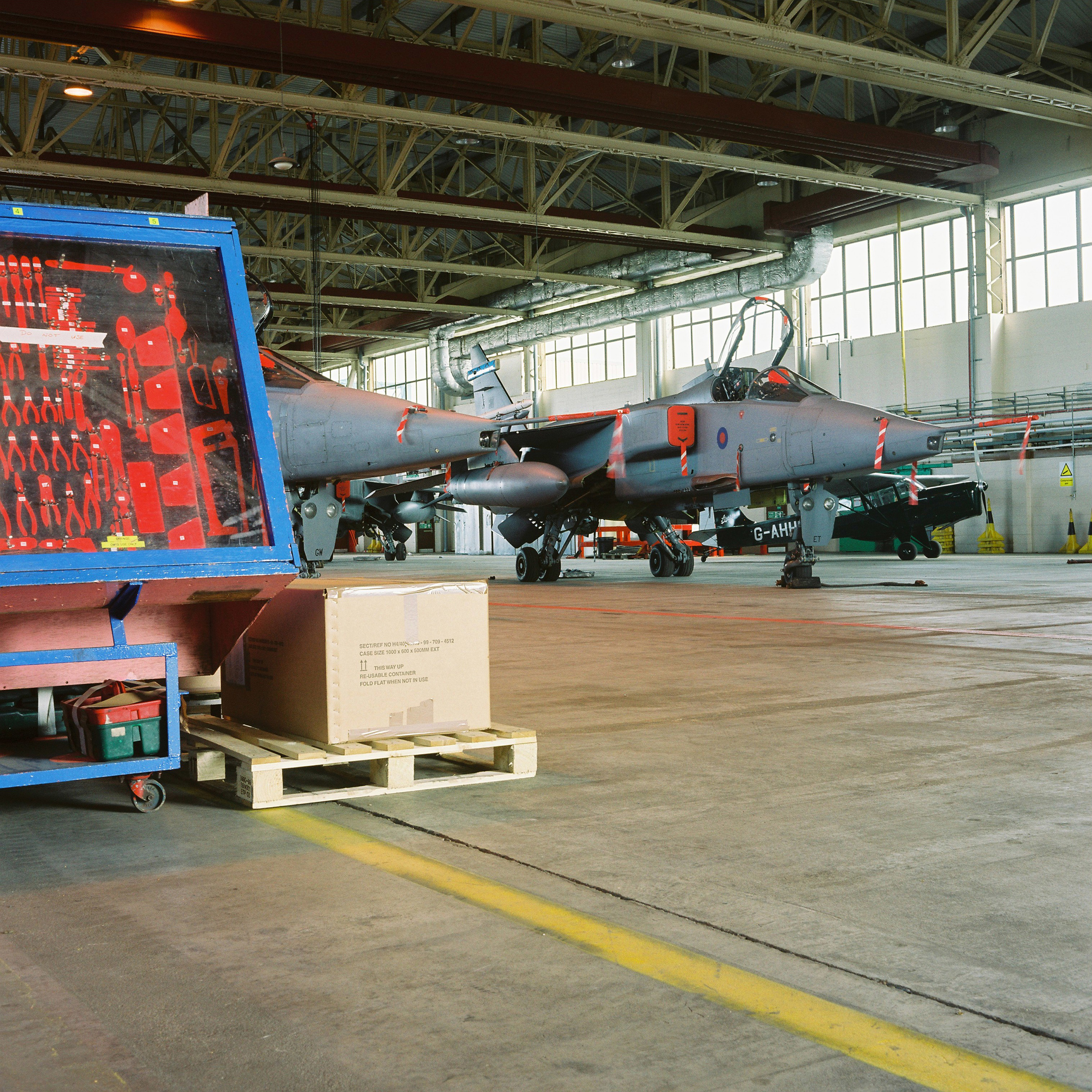 Bright red tools in large blue tool box inside an aircraft hangar with two planes