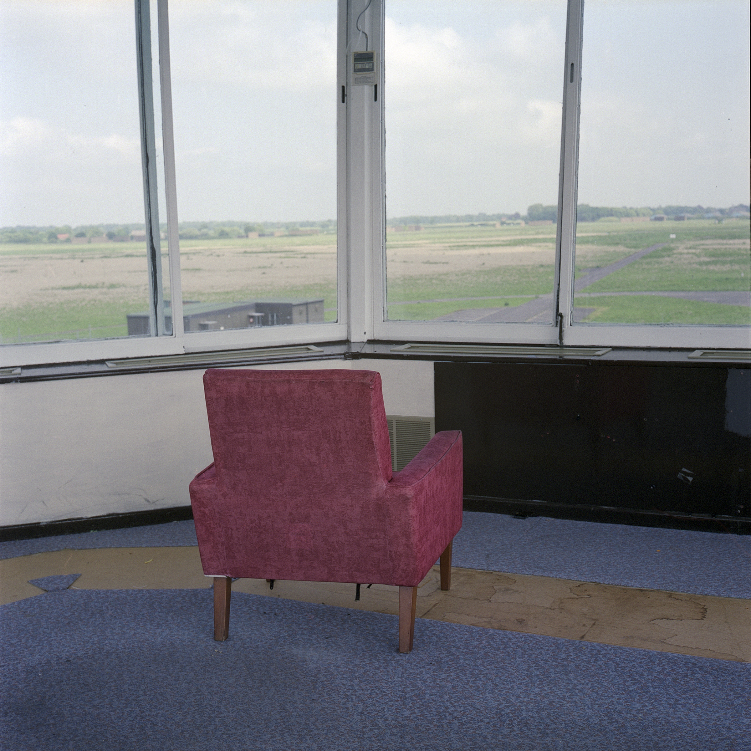 Red chair on blue carpet facing outwards through windows looking out onto airstrip