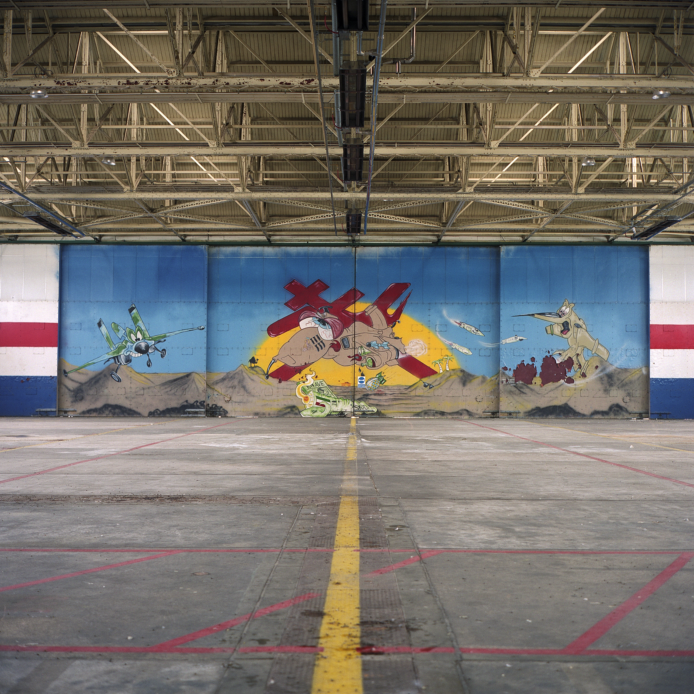 Yellow line (centered), with red lines that criss-cross, draws the eye to a large mural in the background, painted with three cartoon aircaft in hangar. Large central craft is red in from of a yellow sun 