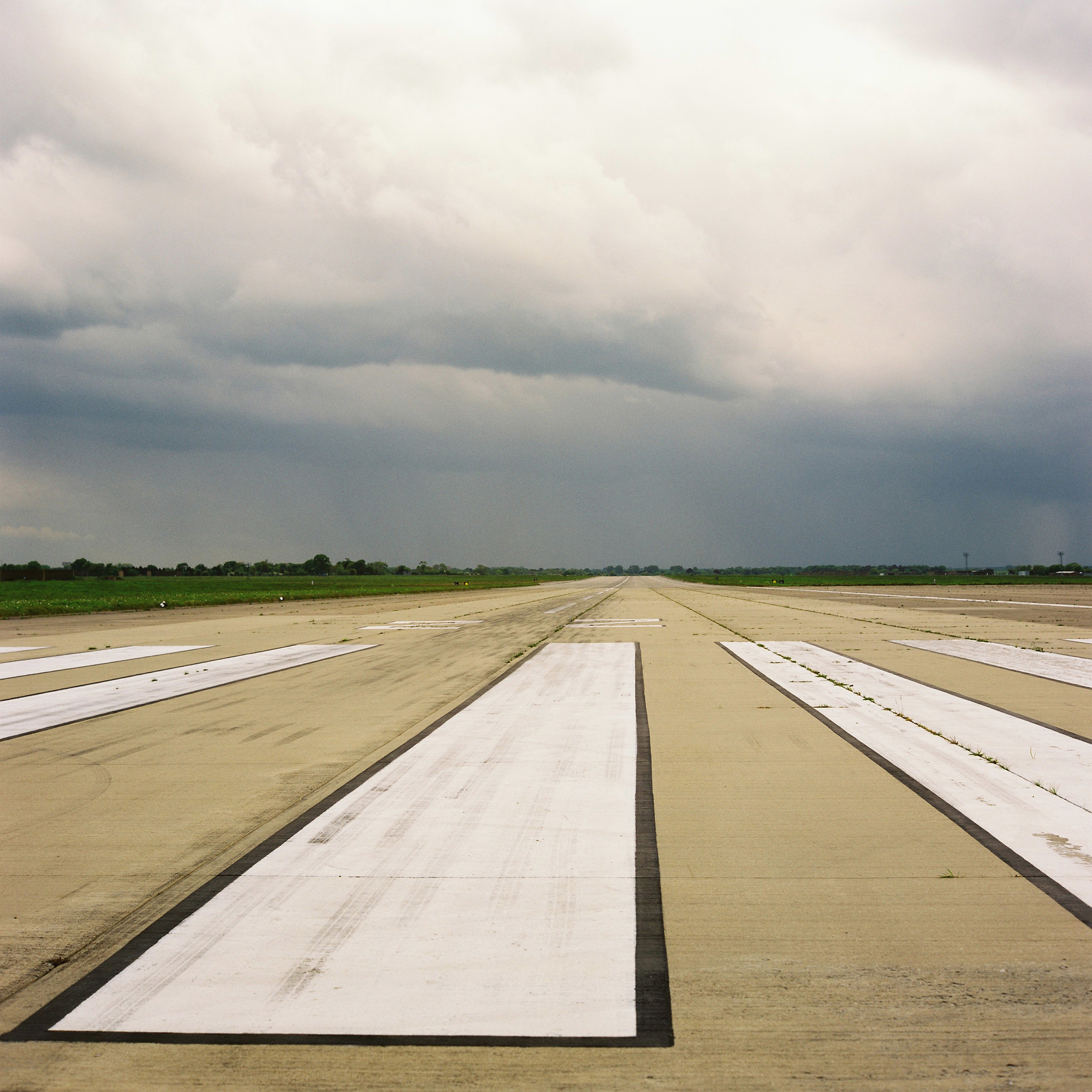 Concrete runway with large white markings fades into vanishing point under a grey cloudy sky