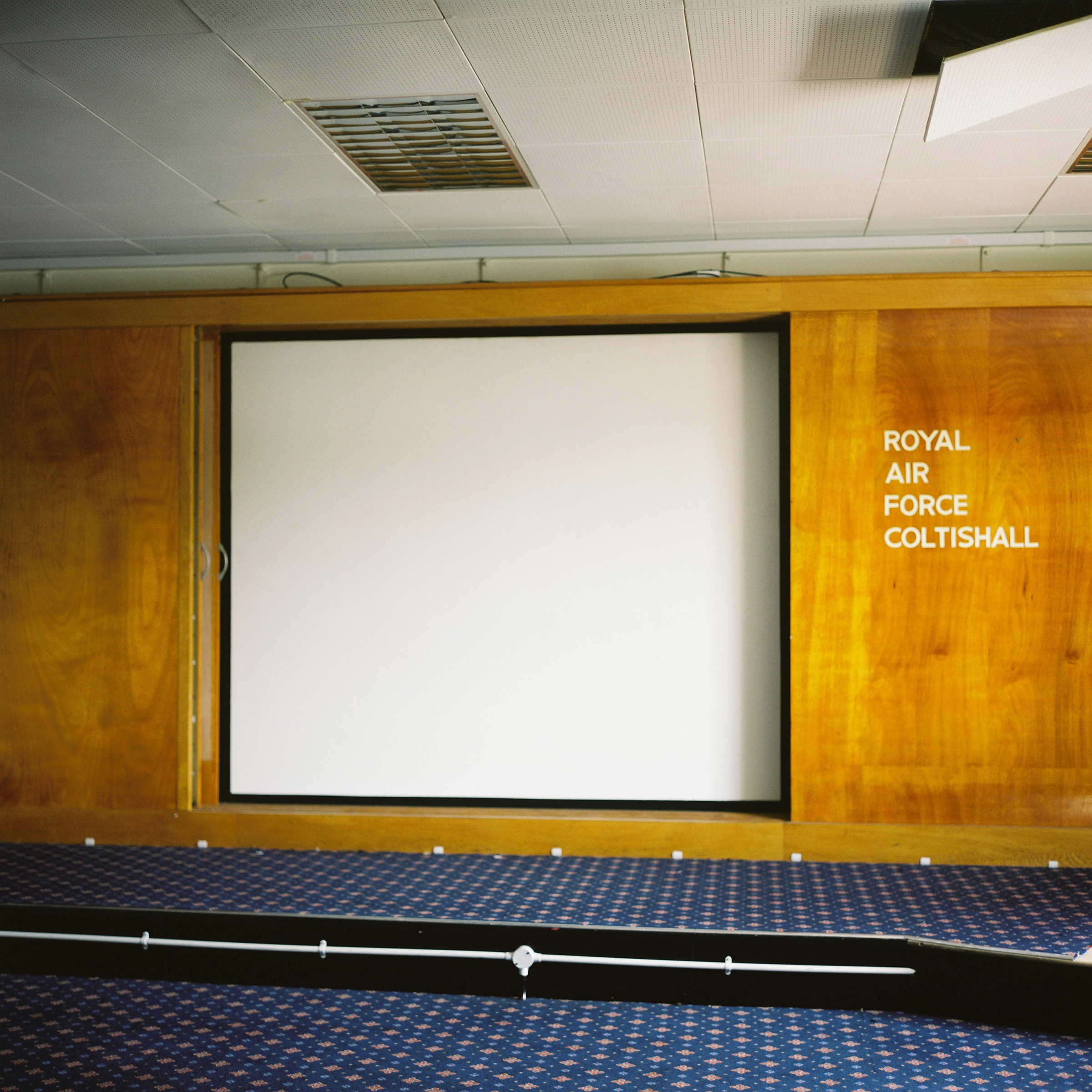 Projector screen set into wooden panelling with blue carpet