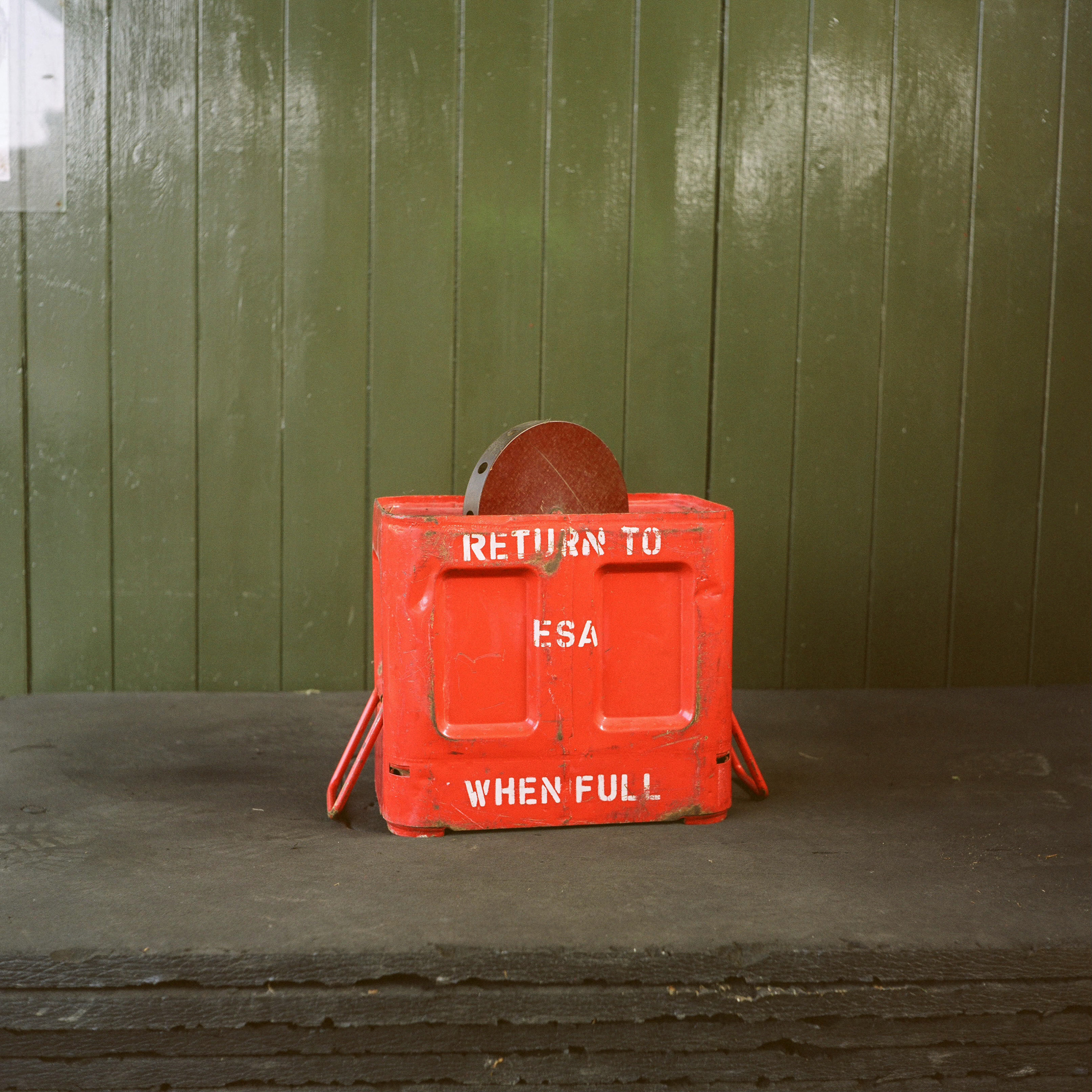 Red metal case in front of green painted wood panelling
