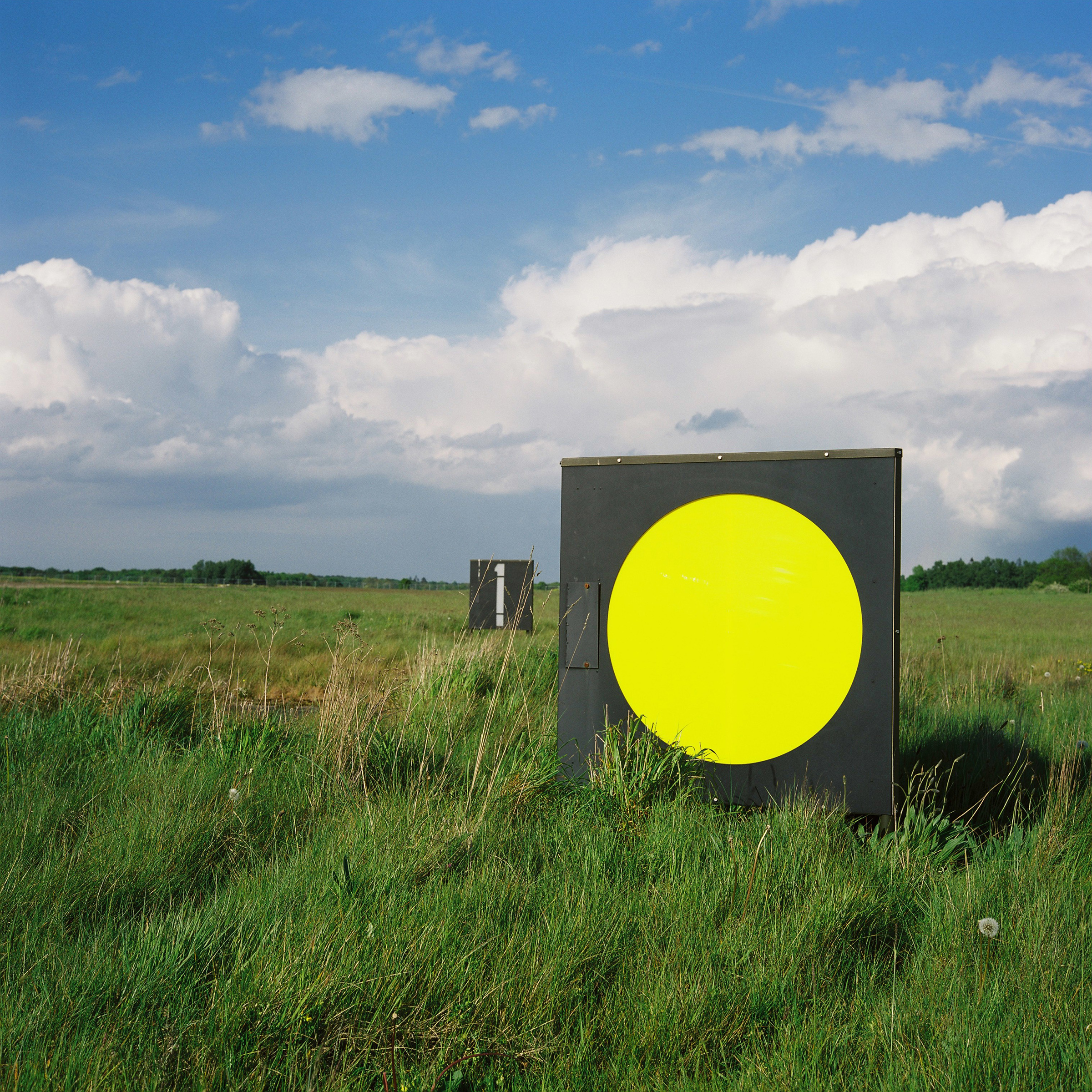 Blue sky with clouds, green grass, square marker with bright yellow circle