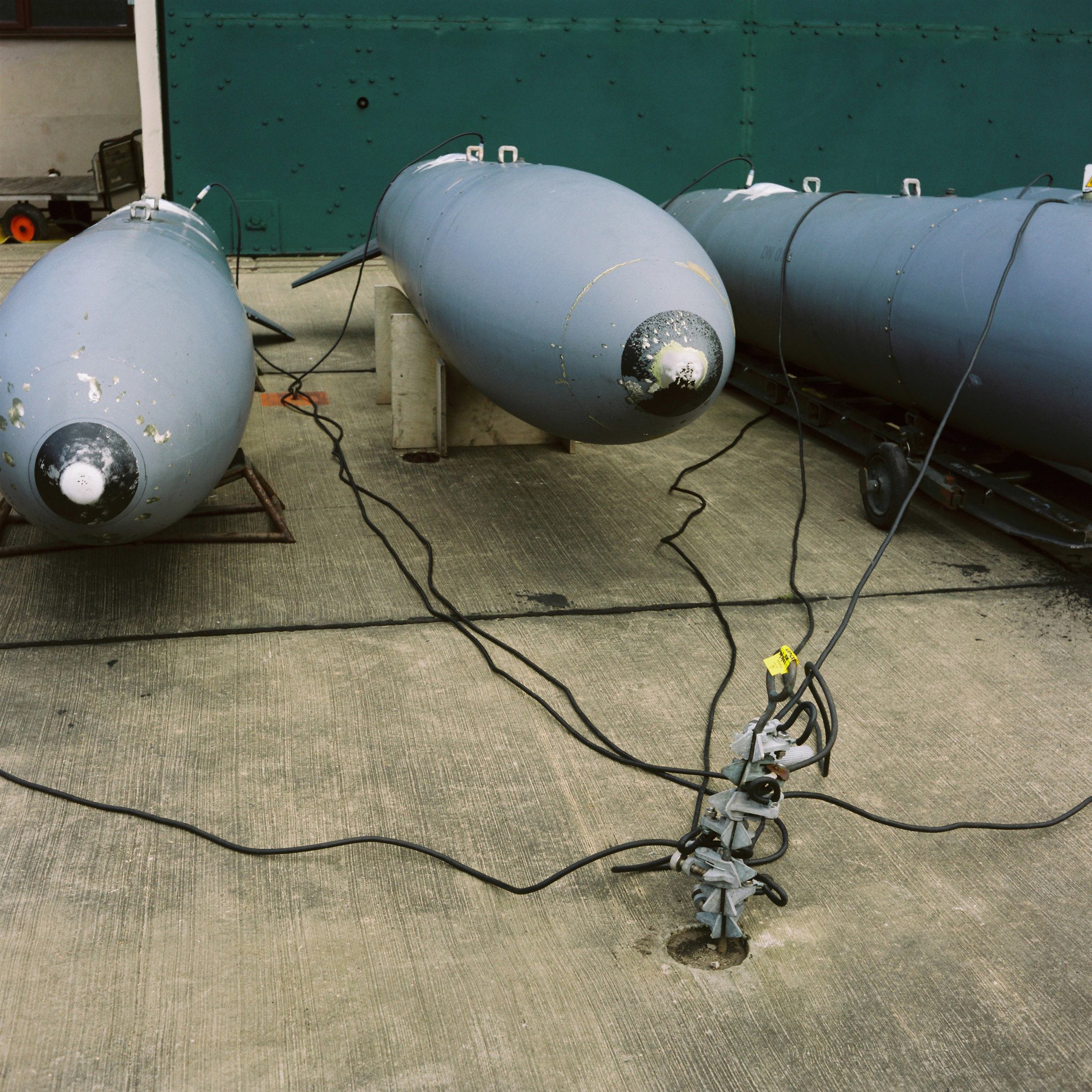 Three large fuel pods (pointing towards viewer) with wires drawn together and plugged into single socket set in concrete