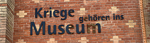 A sign on a brick wall reading: Wars belong in the museum