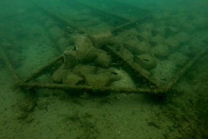 An underwater archaeological site covered by a metal grid structure and surrounded by sandbags
